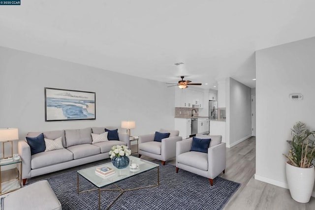 living room featuring ceiling fan, sink, and light wood-type flooring