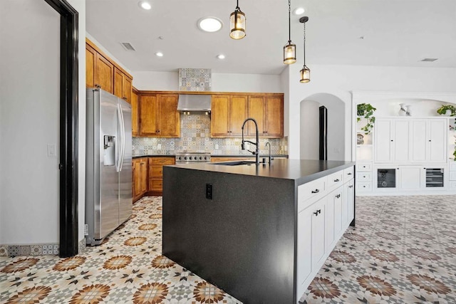 kitchen with tasteful backsplash, hanging light fixtures, range, stainless steel fridge with ice dispenser, and a center island with sink