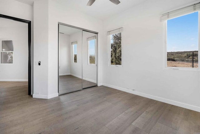 unfurnished bedroom featuring ceiling fan, a closet, multiple windows, and light wood-type flooring