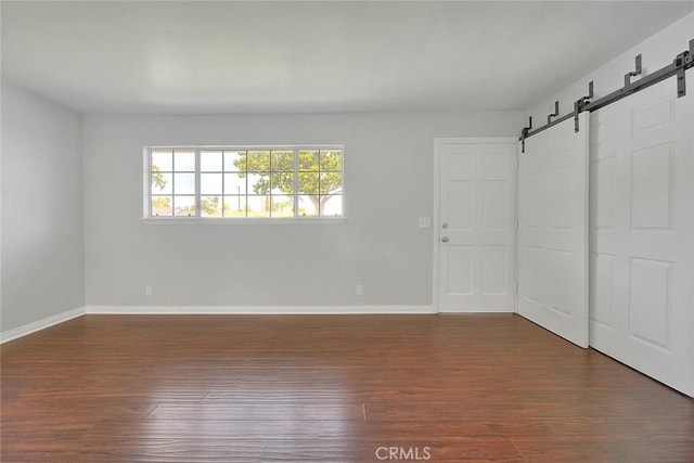 spare room featuring a barn door, baseboards, and dark wood-style flooring