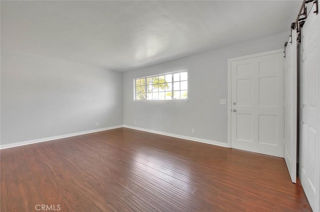 empty room featuring dark wood finished floors, a barn door, and baseboards