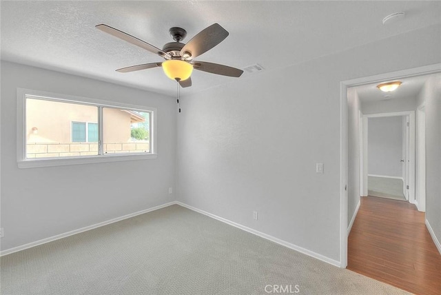 carpeted spare room with visible vents, baseboards, a textured ceiling, and ceiling fan