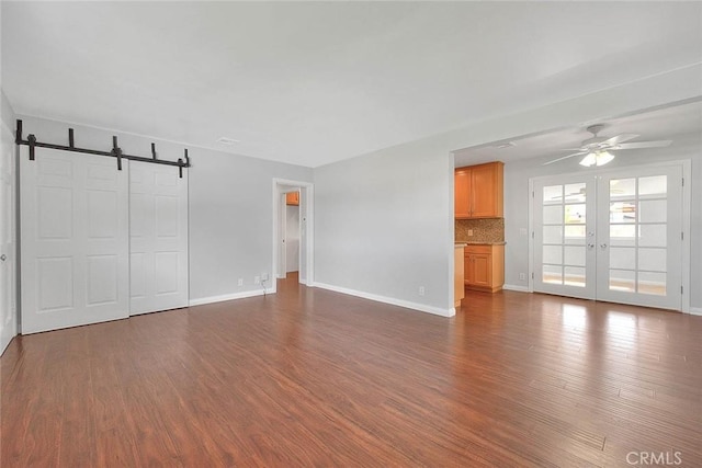 unfurnished living room with ceiling fan, baseboards, a barn door, french doors, and dark wood-style flooring