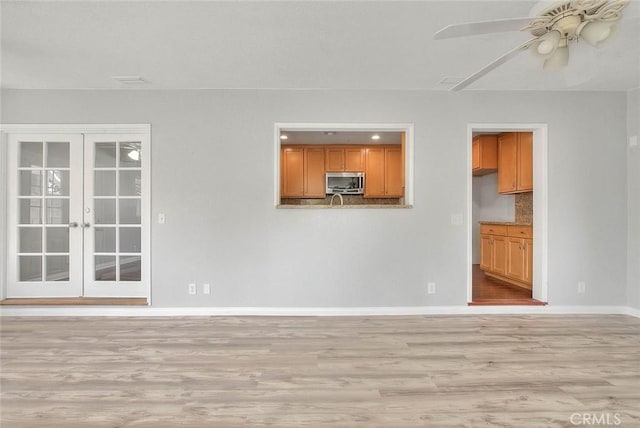 unfurnished living room with a ceiling fan, light wood-style flooring, french doors, and baseboards