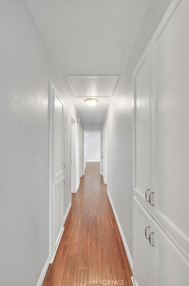 hallway with baseboards, a textured ceiling, dark wood finished floors, and a textured wall