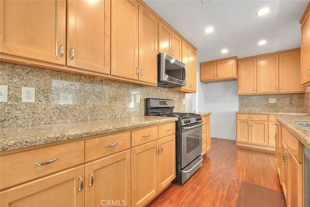 kitchen featuring light wood-type flooring, light stone counters, recessed lighting, stainless steel appliances, and decorative backsplash