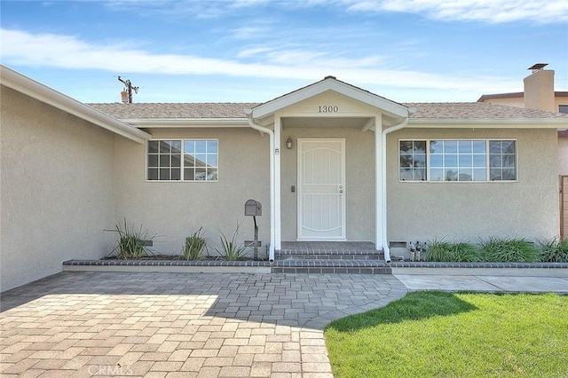 doorway to property with stucco siding and a shingled roof