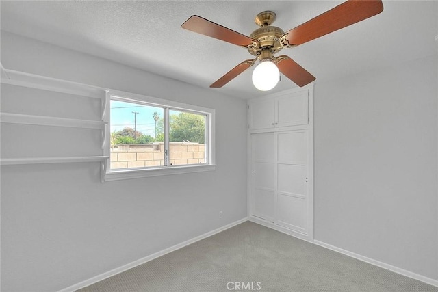 unfurnished bedroom featuring ceiling fan, a textured ceiling, baseboards, and light carpet