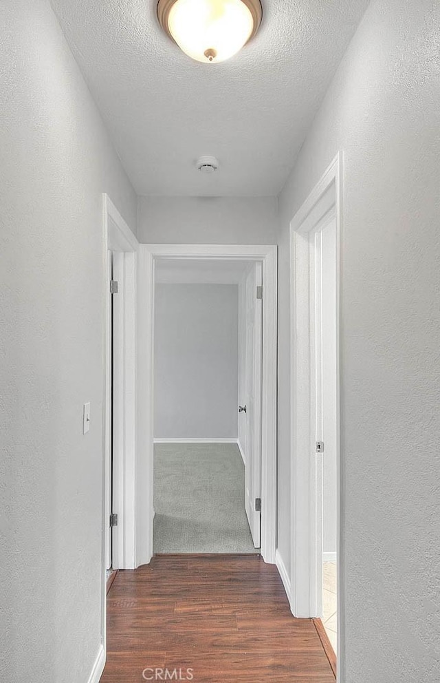 hallway featuring baseboards, a textured ceiling, a textured wall, and wood finished floors