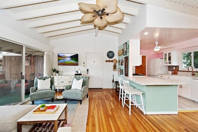 living room featuring sink, vaulted ceiling with beams, light hardwood / wood-style floors, and ceiling fan