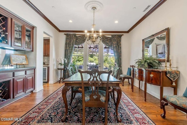 dining room with a notable chandelier, ornamental molding, wine cooler, and light hardwood / wood-style floors