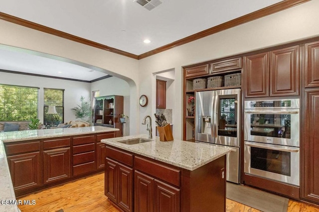 kitchen with sink, crown molding, a kitchen island with sink, stainless steel appliances, and light wood-type flooring