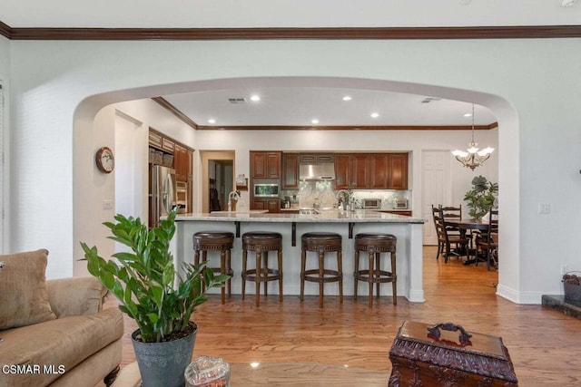 kitchen with a breakfast bar, backsplash, light stone counters, ventilation hood, and light wood-type flooring