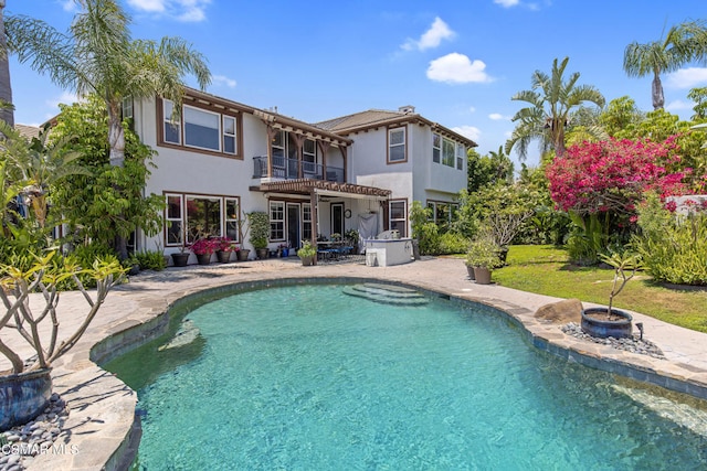 rear view of property featuring a balcony, a pool with hot tub, an outdoor fire pit, and a patio area