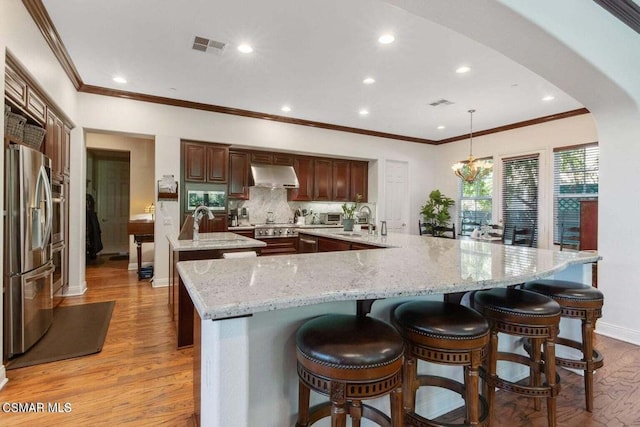 kitchen with appliances with stainless steel finishes, decorative light fixtures, ventilation hood, sink, and a large island