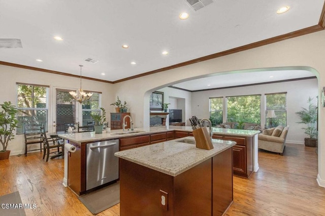 kitchen with stainless steel dishwasher, decorative light fixtures, a center island with sink, and light hardwood / wood-style flooring