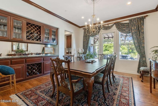 dining room featuring hardwood / wood-style flooring, crown molding, bar area, and a chandelier