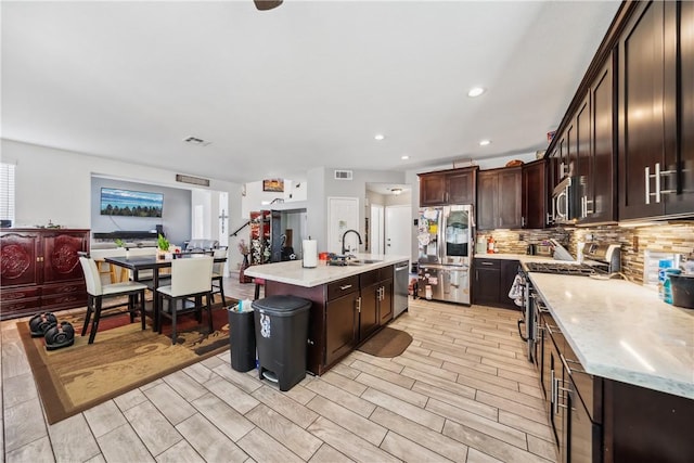 kitchen featuring appliances with stainless steel finishes, sink, a center island with sink, and dark brown cabinetry