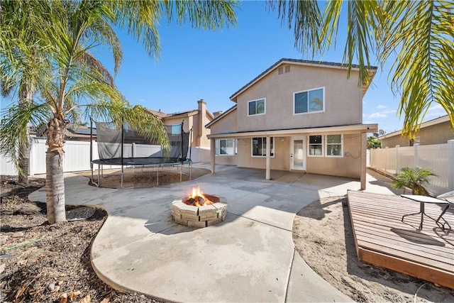 rear view of property featuring a trampoline and a fire pit