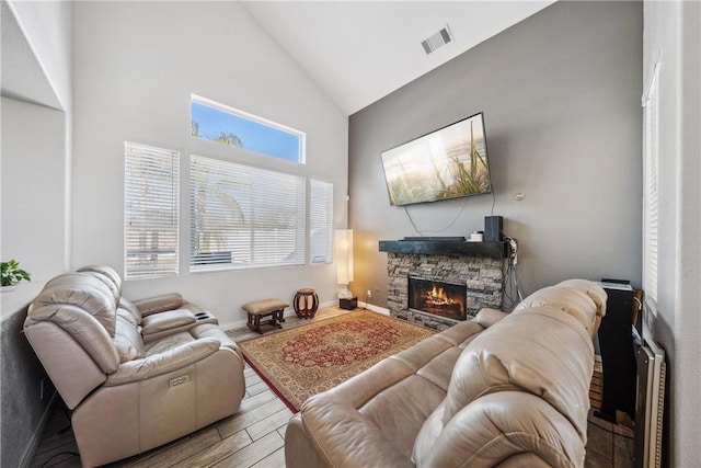 living room with visible vents, a stone fireplace, wood finished floors, high vaulted ceiling, and baseboards