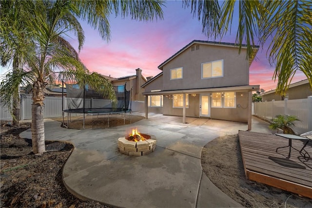 rear view of house with an outdoor fire pit, a fenced backyard, a trampoline, a patio area, and stucco siding