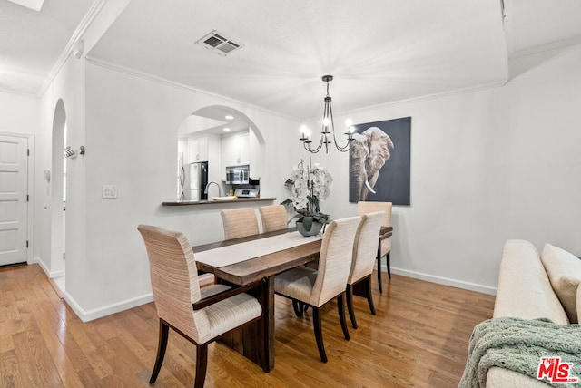 dining area featuring ornamental molding, an inviting chandelier, and light hardwood / wood-style flooring