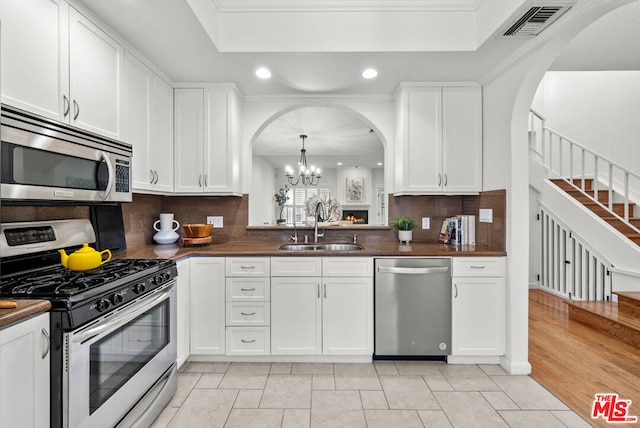 kitchen with white cabinetry, sink, decorative light fixtures, and stainless steel appliances