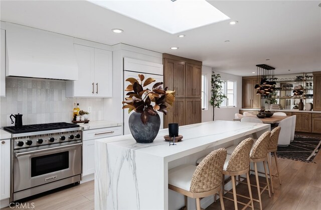 kitchen with backsplash, white cabinets, high end range, a center island, and light wood-type flooring