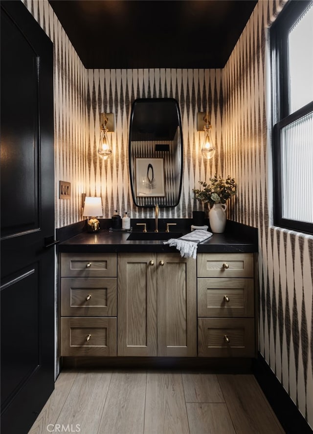 bar with light wood-type flooring, a sink, and wallpapered walls