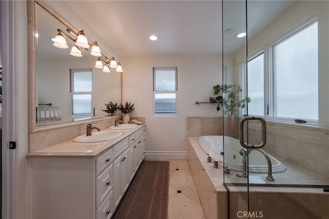 bathroom with a garden tub, double vanity, a sink, and baseboards