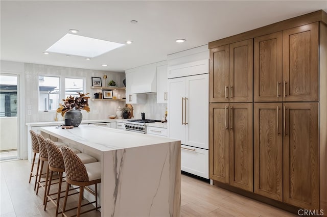 kitchen with a skylight, white cabinets, a center island, open shelves, and high end appliances