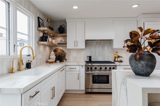 kitchen with sink, white cabinetry, light stone counters, high end stainless steel range oven, and wall chimney range hood