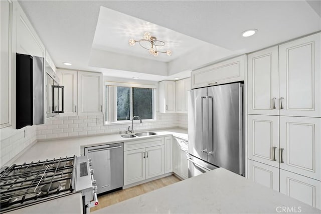 kitchen featuring appliances with stainless steel finishes, tasteful backsplash, white cabinetry, sink, and light hardwood / wood-style flooring