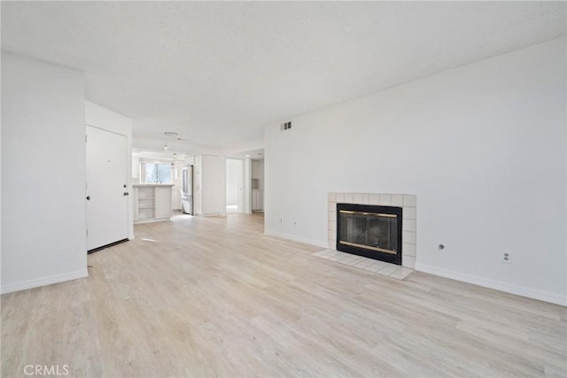 unfurnished living room with a tiled fireplace and light hardwood / wood-style flooring