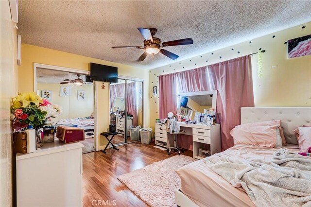 bedroom featuring hardwood / wood-style flooring, ceiling fan, multiple closets, and a textured ceiling