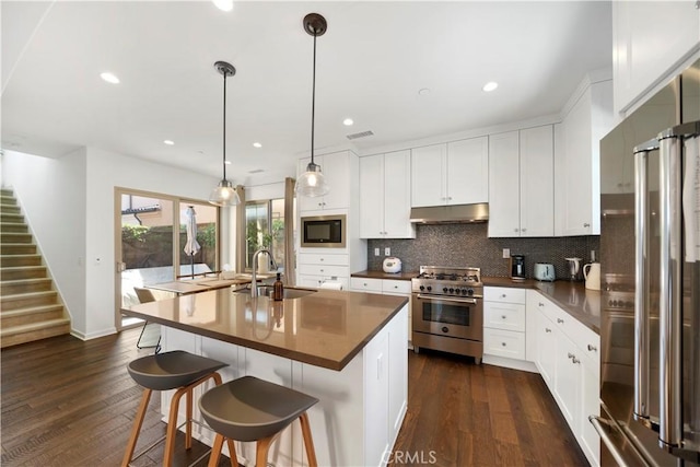 kitchen with pendant lighting, an island with sink, sink, white cabinets, and high end appliances