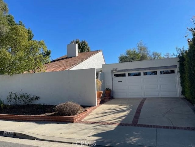 view of side of property with stucco siding, concrete driveway, fence, a garage, and a tiled roof