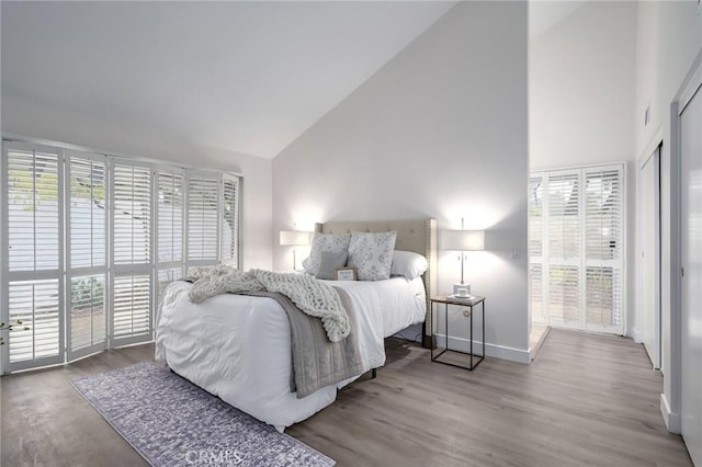 bedroom with high vaulted ceiling, baseboards, and wood finished floors