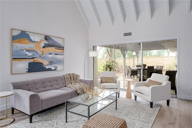 living area with wood finished floors, baseboards, visible vents, high vaulted ceiling, and beam ceiling