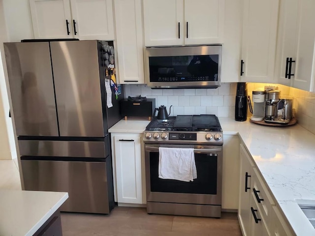 kitchen with white cabinetry, backsplash, stainless steel appliances, and light stone countertops