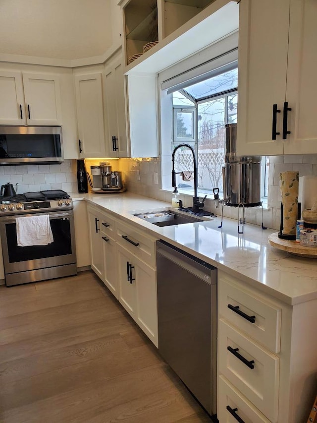 kitchen featuring sink, appliances with stainless steel finishes, white cabinets, light stone countertops, and backsplash