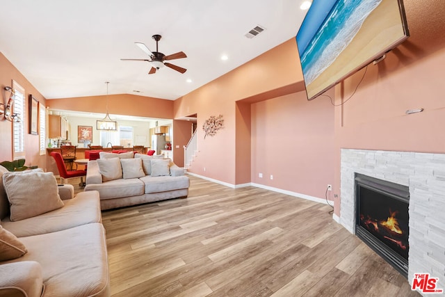 living room with vaulted ceiling, a stone fireplace, ceiling fan, and light hardwood / wood-style floors