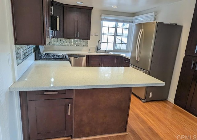 kitchen with sink, light hardwood / wood-style flooring, stainless steel appliances, light stone counters, and kitchen peninsula