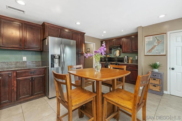 kitchen with light tile patterned flooring, dark stone counters, stainless steel fridge, and range with gas stovetop