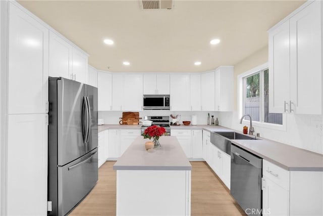 kitchen featuring a kitchen island, sink, white cabinets, stainless steel appliances, and light wood-type flooring