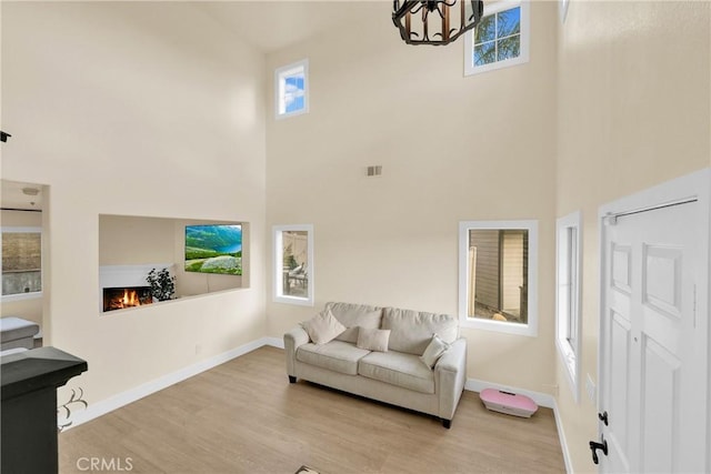 living room with an inviting chandelier, light hardwood / wood-style flooring, and a high ceiling