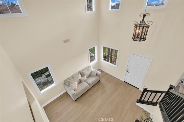 living room featuring an inviting chandelier, a healthy amount of sunlight, light hardwood / wood-style floors, and a high ceiling