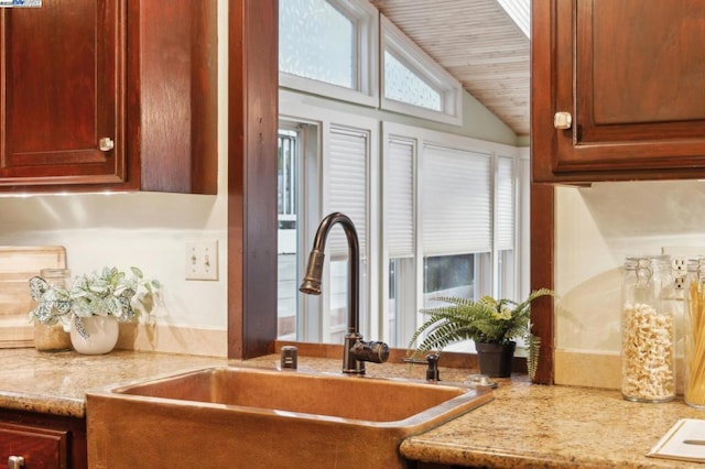 kitchen with lofted ceiling, light stone countertops, and sink