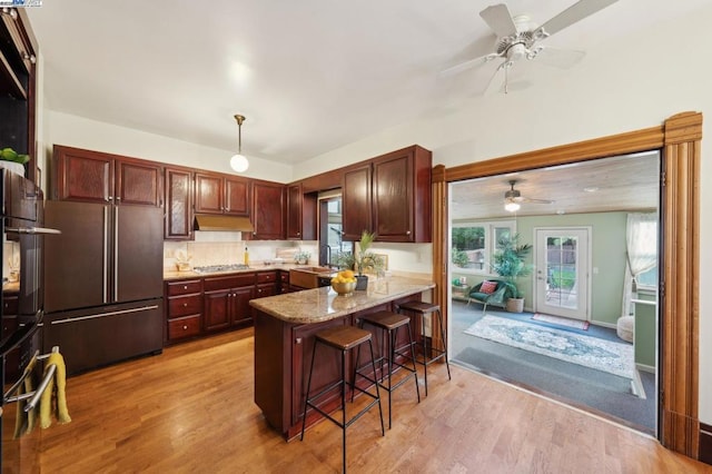 kitchen featuring stainless steel gas cooktop, a breakfast bar area, refrigerator, light hardwood / wood-style flooring, and kitchen peninsula