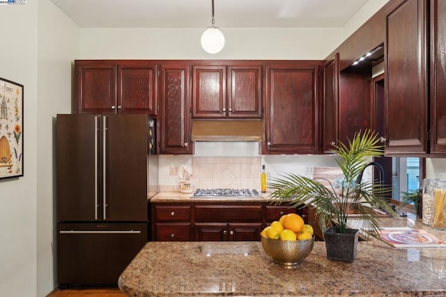 kitchen with pendant lighting, ventilation hood, light stone countertops, high quality fridge, and stainless steel gas stovetop